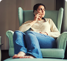 Woman sat inside on an armchair talking on the phone